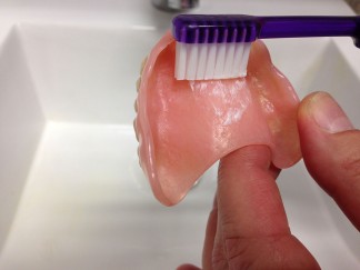 Cleaning the underside of a denture with a toothbrush